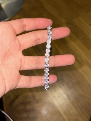 Silverfärgat tennisarmband med stenar - Snyggt tennisarmband i silverfärg med gnistrande, runda vita stenar som sitter tätt i rad. Armbandet har en klassisk och stilren design som passar perfekt till dig som gillar att glänsa lite extra. Låset är diskret och håller armbandet säkert på plats.