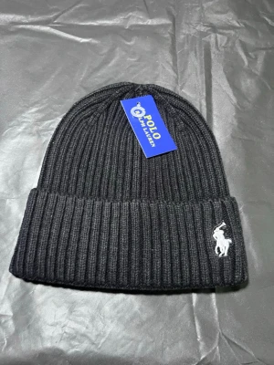 Svart ribbstickad mössa Polo Ralph Lauren - Svart ribbstickad mössa från Polo Ralph Lauren med uppvikt kant och klassisk vit broderad logga framtill. Snygg och enkel design som passar till det mesta. Tillverkad i mjukt och värmande material.