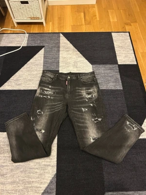 Dsquared jeans - Säljer ett par svarta jeans med slitningar och tvättade detaljer framtill och baktill. Jeansen har fem fickor, raka ben och en klassisk knappgylf. Perfekta för en avslappnad och trendig look.