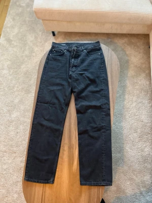 Svarta raka jeans från J.Lindeberg - Svarta jeans från J.Lindeberg i modellen Johnny.  • Storlek: 31/32 (enligt etikett) • Passform: Rak / straight • Skick: Bra begagnat skick, normalt bruksslitage • Färg: Svart • Detaljer: Klassisk 5-ficksdesign, knappgylf, diskret J.Lindeberg-detalj på myntfickan  Stilrena jeans i tidlös modell – enkla att matcha både casual och mer uppklädda outfits.