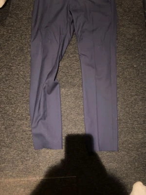 Mörkblå kostym med kavaj och byxor - Snygg mörkblå kostym med klassisk kavaj och matchande byxor. Kavajen har två knappar och fickor med lock. Perfekt för dig som vill ha en stilren och tidlös look. Passar till skjorta och slips för en uppklädd stil. Endast använd en gång så den e i perfekt skick nypris ligger på runt 3500