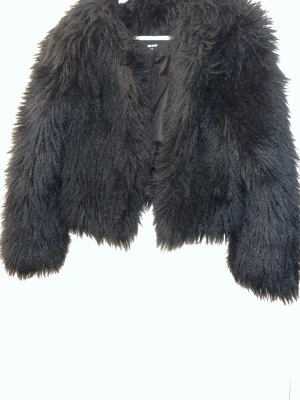 Svart fluffig pälsjacka - Säljer en svart, kort och superfluffig pälsjacka med bred krage och lång luggig pälsimitation. Jackan har en croppad passform och är helfodrad för extra värme. Perfekt för dig som vill sticka ut och hålla dig varm under kalla dagar.