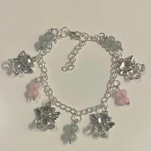 Silverfärgat armband med berlocker - HANDGJORT armband i silver med söta ängelberlocker och små pärlor i ljusblått och rosa. Kedjan har justerbar längd och smidigt lås. 