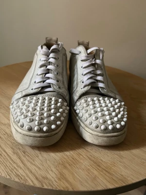 Louboutin junior spiked  - Säljer ett par feta vita loubs junior spiked. Sulorna är som man kan se på bild 4 (där har jag tagit bort inner sulan) fastspikade vilket betyder att skorna garanterat är äkta. De är använda men fortfarande i bra skick och går att tvätta. 