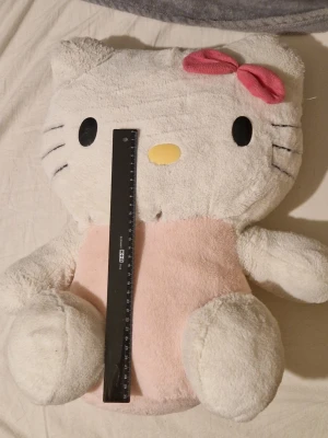 Stor Hello Kitty - Säljer ett stort Hello Kitty mjukisdjur med vit päls, rosa klänning och en rosa rosett på huvudet. Det är ett litet hål som lätt går att laga.