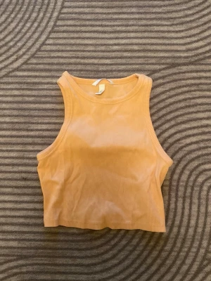 orange ribbad croppad linnetopp 🐈 - Säljer en orange croppad linnetopp med ribbad struktur. Toppen är ärmlös och har en enkel, clean design med rund halsringning. Perfekt att styla till jeans eller kjol för en fräsch look. 🧡