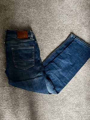 Mörkblå raka jeans från Nudie - Snygga mörkblå jeans från Nudie med raka ben och klassisk femficksdesign. Jeansen har en cool tvätt och detaljer i kontrastsömmar. Skinnpatch med logga bak i midjan. Perfekta för en avslappnad och trendig look.