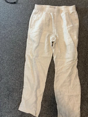 Linnebyxor  - Säljer ett par ljusbeiga linnebyxor med avslappnad passform och resår i midjan. Byxorna har sidofickor och en bakficka, perfekta för en chill och stilren look. Tillverkade i svalt linnematerial som passar perfekt till sommaren. Helt fräscha inte en fläck, knappt använda.
