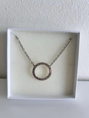 Silverhalsband med cirkelberlock - Efva attling halsband. Ett nyskick halsband i silver med en rund cirkelberlock där texten 'AD ASTRA SIC ITUR' är ingraverad runt hela ringen. Kedjan är tunn och elegant, perfekt för dig som gillar minimalistiska smycken med en personlig touch. Original pris 2500 kr, nu 1600.