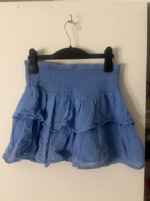 Blå volangkjol med smock - Supersöt blå kortkjol med bred smock i midjan och dubbla volanger från Gina tricot. Storlek 158-164