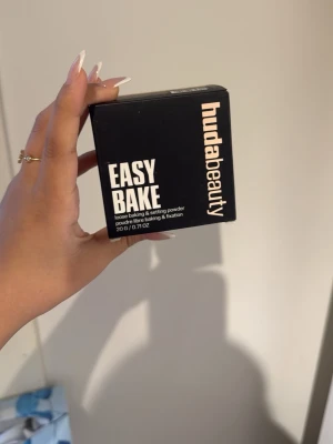 Huda Beauty Easy Bake Pound Cake - Loose baking & setting powder från Huda Beauty i nyansen Pound Cake. Kommer i en svart fyrkantig förpackning med tydlig vit text. Perfekt för att fixera foundation och ge en matt finish. Innehåller 20 g puder.
