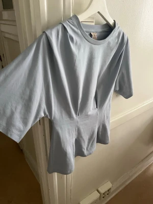 Ljusblå tröja från Nelly - Ljusblå tröja från Nelly ”waist focus tee” där tyget är tight runt midjan och lösare nedanför och vid bröst/axel partiet samt lösa armar. Fint skick, köpt för ca 200kr