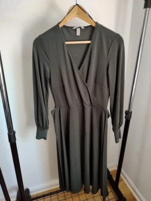 Två långärmade klänningar - Säljer två långklänningar, en i mörkgrått med omlott och v-ringad design samt en svart med enkel rund halsringning. Båda har långärmar och är tillverkade i mjukt syntetmaterial som känns skönt mot huden. Perfekt för dig som gillar stilrena och klassiska plagg.