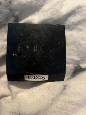 Isadora lila ögonskuggepalett - Säljer en klassisk svart fyrkantig ögonskuggepalett från Isadora. Förpackningen är kompakt och smidig att ta med i väskan. Perfekt för dig som gillar stilrena och enkla produkter. Materialet är hårdplast med en tydlig Isadora-logga på framsidan. Spegeln fungerar ville inte visa ansiktet.