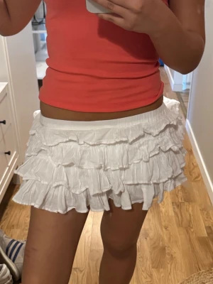 Vit volangkjol med resårmidja - Supersöt kort vit kjol med flera lager volanger och bred resår i midjan och inbyggda shorts. Dom är ganska skyrunkliha men går enklare att göra volangrena fina igen med strykjärn💖