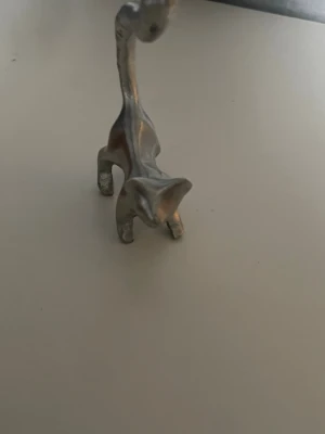Dekorativ giraff i silverfärgad metall - Säljer en stilren och dekorativ giraff i silverfärgad metall. Figurinens design är minimalistisk med mjuka former och lång hals, perfekt som prydnad på hyllan eller skrivbordet. Passar dig som gillar djurmotiv och modern inredning.