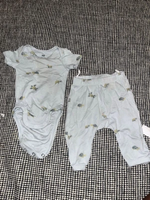 Ljusblått bodyset med sköldpaddor H&M - Sött tvådelat set från H&M med ljusblå body och matchande byxor. Båda delarna har ett gulligt sköldpaddsmönster och bodyn har korta ärmar samt tryckknappar i grenen. Mjukt och bekvämt material, perfekt för små barn.