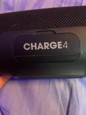 JBL Charge 4 trådlös högtalare svart - Snygg och kraftfull JBL Charge 4 trådlös högtalare i svart. Högtalaren har en robust cylinderformad design med tygmaterial runt om och gummerade ändar. Utrustad med Bluetooth, tydliga knappar för styrning och laddningsport. Perfekt för att streama musik trådlöst.