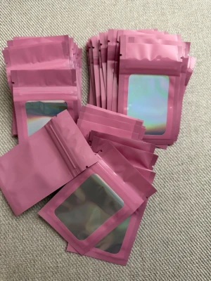 50 stycken Rosa zip-påsar med fönster, 10x6 - 50 stycken rosa zip-påsar i plast med genomskinligt holografiskt fönster på framsidan. Perfekta för förvaring av småsaker, smycken eller presenter. Påsarna är återförslutningsbara och har en modern look. Storlek: 10x6