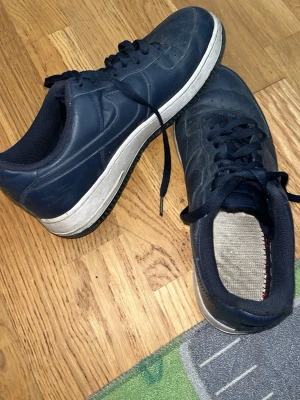 Mörkblå sneakers med vit sula - Snygga mörkblå sneakers med klassisk vit sula och svarta skosnören. Skorna har en låg profil och är tillverkade i syntetmaterial med textilfoder. Perfekta för en avslappnad streetwear-look.