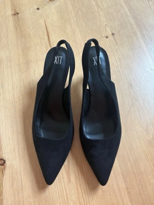 Svarta klackar - Stilrena svarta pumps från XIT med spetsig tå och öppen häl med slingback-rem. Skorna har en smal klack och är klädda i mockaimitation. Aldrig använda!