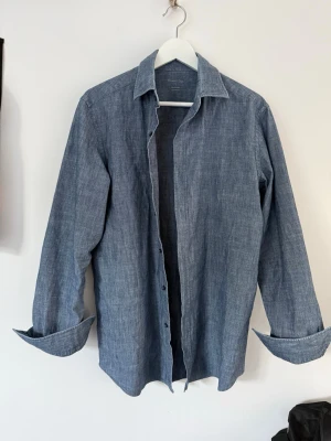 Blå jeansskjorta från Massimo Dutti - Snygg blå skjorta från Massimo Dutti i jeansmaterial. Skjortan har klassisk krage, knappar framtill och långa ärmar. Perfekt för en avslappnad men stilren look. Enkel att matcha med både jeans och chinos.