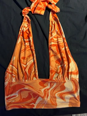Orange swirl halterneck topp - Säljer en snygg halterneck topp med knyt i nacken och ett färgstarkt mönster i orange Toppen är croppad och har djup urringning