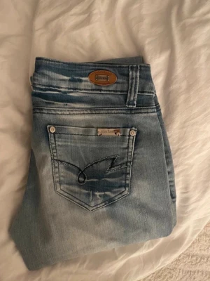 Ljusblå jeans från Miss Rosina - Säljer ett par ljusblå jeans från Miss Rosina med snygga slitningar och dekorativ söm på bakfickan. Jeansen har klassisk femficksmodell, silverfärgade detaljer och patch i läderimitation vid linningen. Perfekta för en avslappnad och trendig look.