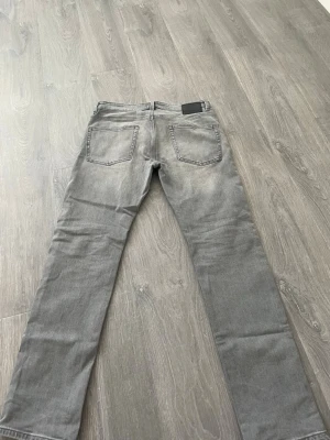 Grå raka jeans med tvättad look - Säljer ett par grå jeans med rak passform och tvättad effekt. Jeansen har två bakfickor och klassisk femficksdesign. Materialet är denim och färgen är en snygg grå nyans som passar till det mesta. Perfekta för dig som gillar en avslappnad stil.