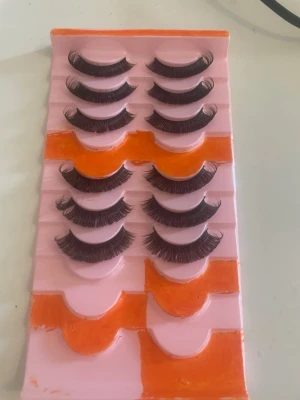 Svarta volymfransar i multipack - Säljer ett set med sex par svarta lösögonfransar i volymmodell. Fransarna har en böjd form och sitter på en rosa och orange bricka. Perfekta för att skapa en dramatisk look till läppsminkningen.,säljer för dem passar inte riktigt mig