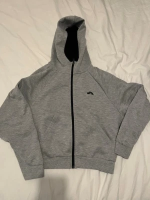 Grå zip hoodie från J.Lindeberg - Snygg grå hoodie med dragkedja från J.Lindeberg. Klassisk passform med huva och ribbade muddar. Liten svart logga på bröstet och två fickor framtill. Tillverkad i mjukt bomullsmaterial som känns skönt mot huden.💕