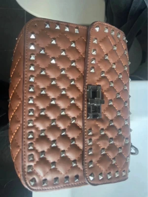 Valentino Garavani rockstud väska  - Snygg brun axelväska med quiltat mönster och silverfärgade nitar. Väskan har en metallkedja som axelrem och ett vridlås framtill. Perfekt för dig som gillar edgy detaljer och vill sticka ut lite extra.