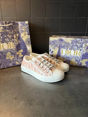 Dior skor  - Säljer ett par snygga Dior Oblique sneakers i vitt och ljusrosa med klassiskt monogrammönster. Skorna har vita snören, robust vit sula och detaljer med 'Christian Dior' på plösen. Perfekta för dig som vill ha något exklusivt och trendigt. Storlek 38
