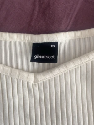 Vit ribbad topp från Gina Tricot - Snygg vit ribbad topp från Gina Tricot i storlek XS. Toppen har v-ringning och offshoulder-design med smala axelband. Perfekt att styla med jeans eller kjol för en trendig look. Har aldrig använts.