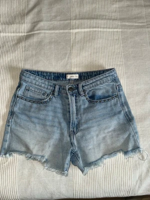 Ljusblå jeansshorts med pärldetaljer - Snygga ljusblå jeansshorts från Mango med pärldetaljer längs fickorna framtill.