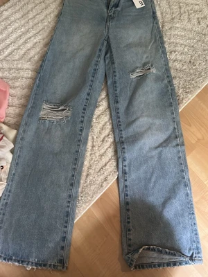 Blåa wide leg jeans från 157 - Säljer ett par ljusblå wide leg jeans från 157 med slitna detaljer på benen och rå kant längst ner. Jeansen har hög midja och klassisk femficksdesign. Perfekta för dig som gillar en avslappnad och trendig look.