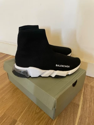 Balenciaga Speed Trainer svarta sneakers - Svarta Balenciaga Speed Trainer sneakers med stickad ovandel i textil, vit chunky sula och tydlig logga på sidan. Skorna har en strumpliknande passform och transparent detalj i hälen. Perfekta för dig som gillar streetwear och modern design.