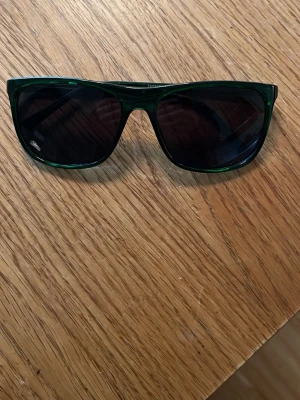 Gröna solglasögon med retroform - Snygga solglasögon i mörkgrönt med klassisk retroinspirerad form. Bågarna är tillverkade i syntetmaterial och har en stilren look som passar perfekt till sommaren. En cool accessoar för dig som vill sticka ut lite extra.