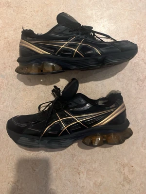 Svarta Asics - guldiga skor - Säljer ett par svarta Asics sneakers begagnade använda ett tag kvitto och sko kartong finns.