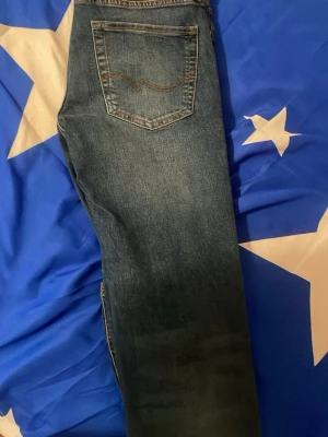 Blå jeans från Jack & Jones - Säljer ett par klassiska blå jeans från Jack & Jones jeans med snyggt slitna detaljer och kontrastsömmar. Jeansen har en bakficka med  karakteristiska broderi och är tillverkade i denim. Perfekta för en avslappnad och trendig look.