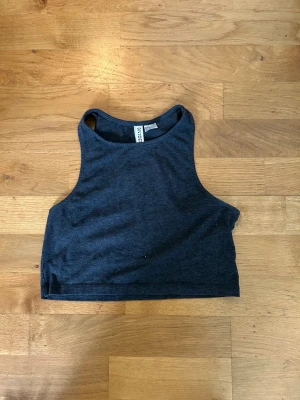 Mörkgrå croppad linnetopp - Snygg mörkgrå croppad linnetopp från H&M. Toppen är ärmlös och har en enkel, stilren design med hög halsringning. Använd och i fint skick. Storlek XS. 