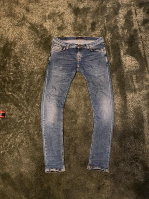 Blå slim fit jeans med slitningar - Säljer ett par blå slim fit jeans med lätt slitna detaljer och klassisk femficksdesign. Jeansen har en smal passform och är tillverkade i denim med stretch för extra komfort. Perfekta för en avslappnad och trendig look.