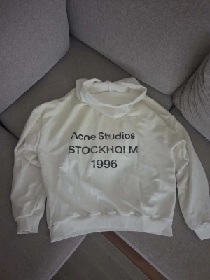 Vit hoodie Acne Studios Stockholm S - Säljer en vit hoodie från Acne Studios med trycket 'Acne Studios STOCKHOLM 1996' på bröstet. Hoodien har en klassisk passform med huva och ribbade muddar vid ärmar och nederkant. Tillverkad i mjukt material som känns skönt mot huden.