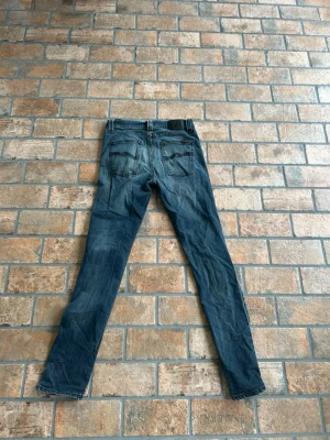 Blå slim fit jeans från Nudie jeans - Säljer ett par blå slim fit jeans från nudie med klassisk femficksmodell och snygga slitningar. W30 och L32 Jeansen har normalhög midja och smala ben, perfekt för en trendig och avslappnad look. Materialet är mjukt denim med lite stretch.