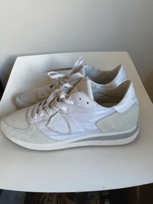 Vita sneakers från Philippe Model - Stilrena vita sneakers från Philippe Model med ovandel i mocka, mesh och läderdetaljer. Klassisk låg modell med vita skosnören och diskret logga på plösen. Perfekta för en clean och modern look.