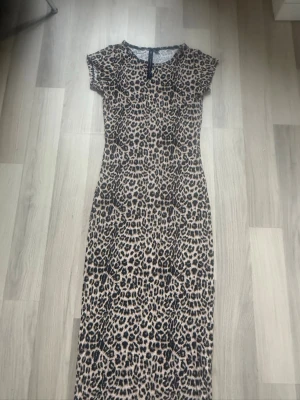 Leopardmönstrad långklänning - Säljer en snygg långklänning med leopardmönster från Lager 157. Klänningen har korta ärmar och en figurnära passform. Materialet är mjukt och stretchigt. Endast provad.