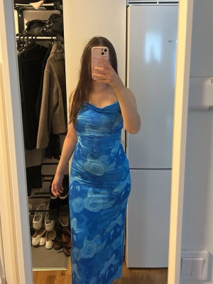 Blå långklänning med rosor - Jag säljer denna fina blåa klänning som framhäver kroppens form perfekt. Den är lång med en knytning baktill och är gjord i ett otroligt bekvämt material. Passar både S och M och är i mycket bra skick. 