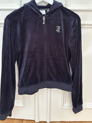 Mörkgrå velour hoodie Juicy Couture - Säljer en mjuk och lyxig mörkgrå velour hoodie från Juicy Couture med dragkedja och fickor framtill. Har huva och ett glittrande JC-logotyp i strass på bröstet. Perfekt för en chill och Y2k look ❤️🤗. 