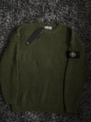 Olivgrön stickad tröja Stone Island - Säljer en olivgrön stickad tröja från Stone Island med klassisk patch på ärmen. Tröjan har rund halsringning och ribbade muddar vid ärmslut och nederkant. Perfekt för dig som gillar streetwear och vill ha något både snyggt och bekvämt.