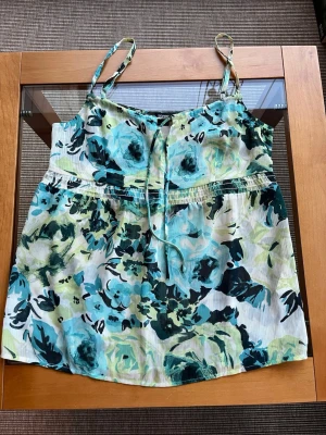 Blommigt linne från Esprit, Storlek 32/34. - Supersött linne från Esprit med blommigt mönster i blått, grönt och vitt. Tunt, luftigt tyg med smala reglerbara axelband. Knyts framtill.  Storlek 32/34. 